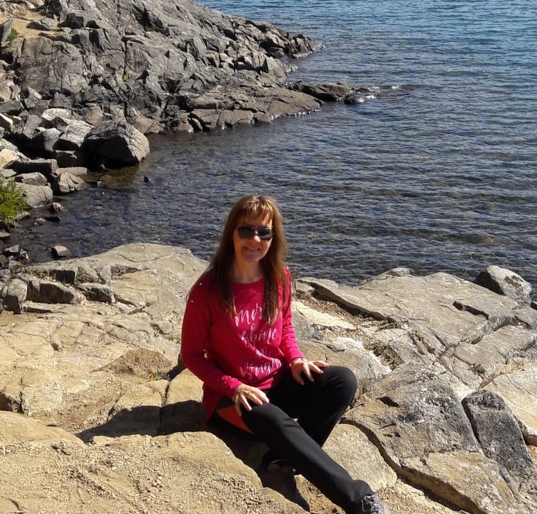 imagen de la consultora sentada sobre una roca, al costado de un lago. Sonríe
